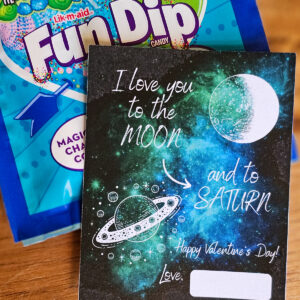 Valentine Card that reads, I love you to the moon and to Saturn. Black background with white lettering and white moon and Saturn graphics. Blue and Green galaxy.